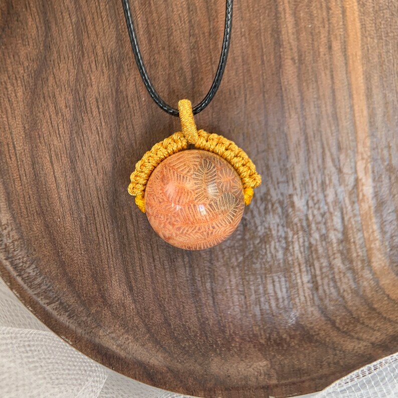 Puede incluir: Un collar de cord&oacute;n dorado con un colgante redondo de coral fosilizado rosa y marr&oacute;n.