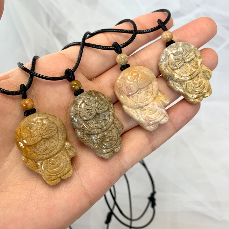 May include: Four necklaces with brown cord and carved stone pendants in the shape of a cartoon character. The pendants are in shades of brown, beige, and light pink.