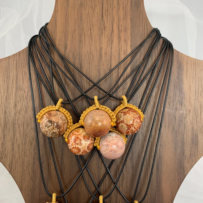 Puede incluir: Cinco collares con colgantes de coral marr&oacute;n y rosa en cordones negros. Los cordones est&aacute;n anudados en estilo macram&eacute; con detalles dorados.