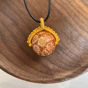 Puede incluir: Un collar dorado y marr&oacute;n con un colgante redondo con un patr&oacute;n floral. El colgante est&aacute; rodeado por un cord&oacute;n amarillo.