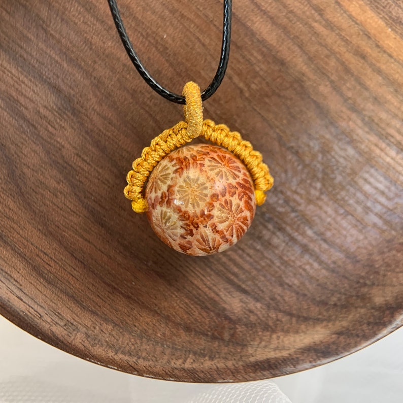 Puede incluir: Un collar dorado y marr&oacute;n con un colgante redondo con un patr&oacute;n floral. El colgante est&aacute; rodeado por un cord&oacute;n amarillo.