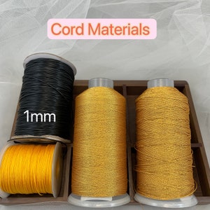 Puede incluir: Tres carretes de cord&oacute;n en una caja de madera. Los carretes son negro, dorado y amarillo. El carrete negro tiene una etiqueta que dice "1 mm".