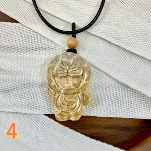 May include: A necklace featuring a brown wooden bead and a pendant crafted from fossilised coral, shaped like a cartoon character. The pendant is translucent and boasts a detailed design.