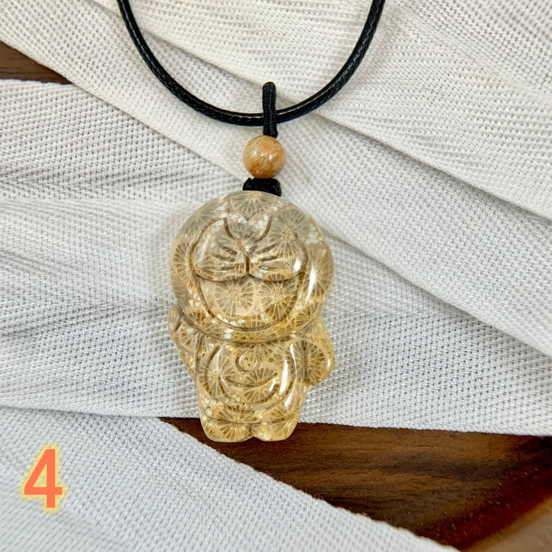 May include: A necklace featuring a brown wooden bead and a pendant crafted from fossilised coral, shaped like a cartoon character. The pendant is translucent and boasts a detailed design.