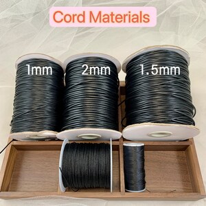 May include: Three spools of black cord in a wooden box. The spools are labelled 1mm, 2mm, and 1.5mm.
