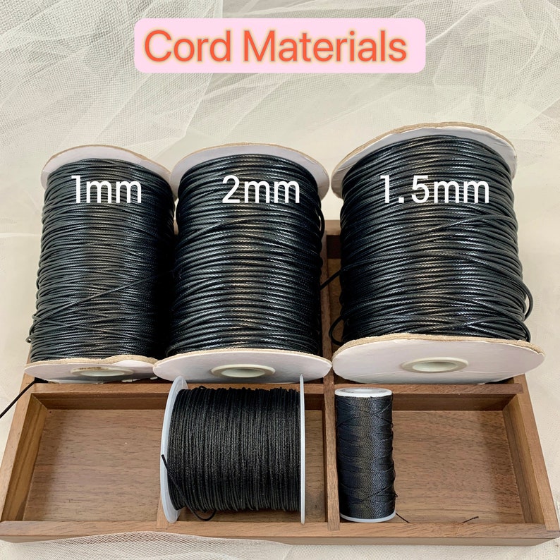 May include: Three spools of black cord in a wooden box. The spools are labelled 1mm, 2mm, and 1.5mm.