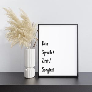 Könnte beinhalten: Ein schwarzer gerahmter Poster mit weißem Hintergrund und schwarzem Text, der "Dein Spruch / Zitat / Songtext" lautet. Der Poster liegt auf einer schwarzen Oberfläche mit einer Vase mit getrocknetem Pampasgras.