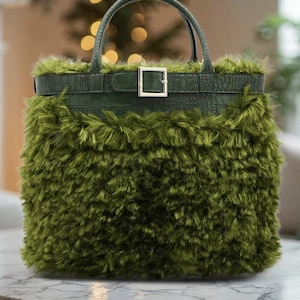 Puede incluir: Un bolso verde con exterior de piel sintética y ribete de cuero con textura de cocodrilo. El bolso tiene un asa superior y un cierre de hebilla. El bolso está sobre una superficie de mármol.