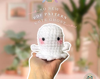 May include: A white crocheted ghost with pink cheeks and black eyes. The ghost is being held in a hand. The text "NO SEW PDF PATTERN CUTE GHOST" is written above the ghost.