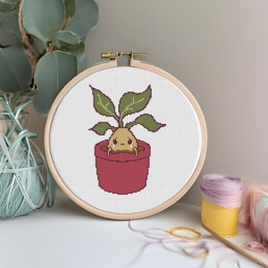 Peut inclure: Un cerceau de broderie au point de croix avec une illustration de dessin animé mignonne d'une plante en pot triste avec des racines brunes et des feuilles vertes. La plante est dans un pot rouge.