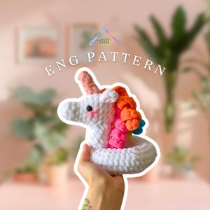 May include: A white crocheted unicorn with a rainbow mane and a pink horn. The unicorn is holding a white crocheted ring.