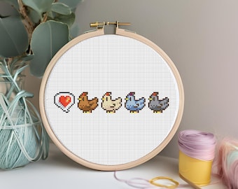 May include: A white embroidery hoop with a cross-stitch design of five pixelated chickens. The chickens are brown, white, blue, and gray. A red heart with a white outline is in a speech bubble to the left of the chickens.