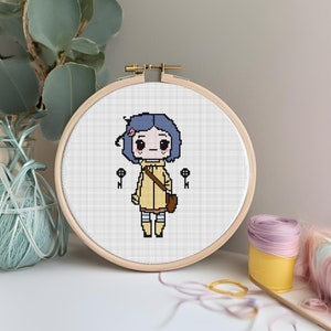 May include: A cross-stitch embroidery hoop featuring a pixelated cartoon character with blue hair, a yellow coat, and a brown satchel. Two black keys flank the character. The embroidery is set in a wooden hoop.