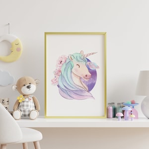 May include: A framed watercolour print of a unicorn with a light blue mane and a pink and purple background. The unicorn is smiling and surrounded by pink flowers. The print is in a gold frame and is displayed on a white shelf with other decorative items.