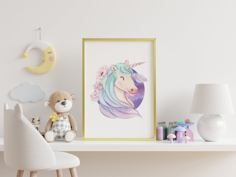 May include: A framed watercolour print of a unicorn with a light blue mane and a pink and purple background. The unicorn is smiling and surrounded by pink flowers. The print is in a gold frame and is displayed on a white shelf with other decorative items.
