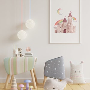 May include: A framed watercolour print of a castle with a rainbow and moon hangs on a white wall. A child's room is furnished with a striped table, a star-patterned chair, and a whale-shaped pillow. Decorative lamps hang from the ceiling.