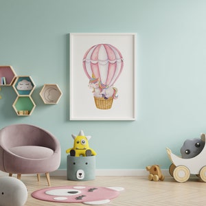 May include: A framed watercolour print of a unicorn in a hot air balloon, with pink and white stripes. The nursery decor includes a pink chair, stuffed animals, and wooden toys, creating a whimsical atmosphere.