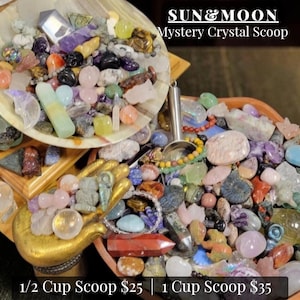 May include: A collection of assorted polished crystals, gemstones, and carved stone figures in various shapes and colors, including a metal scoop, a gold-colored hand-shaped dish, and a bowl, with text reading SUN & MOON Mystery Crystal Scoop.