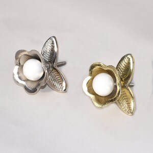 May include: Two decorative flower-shaped cabinet knobs with a white pearl centre. One knob is silver and the other is gold.