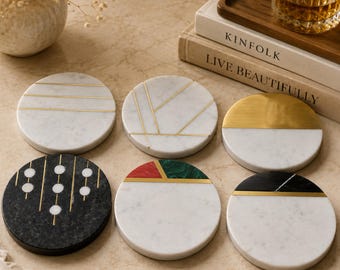 May include: A set of six circular coasters made of white, black, green, and red marble with inlaid gold-tone metal accents. The designs include horizontal lines, geometric patterns, solid color blocking, and vertical lines with circular motifs.