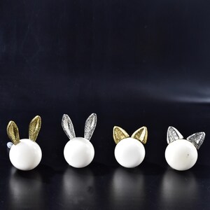 May include: Four white ceramic bunny door knobs with gold and silver accents. The knobs are round and have a smooth finish.