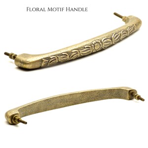 May include: Two antique brass cabinet handles. The top handle features a floral motif design, while the bottom handle is a simpler, solid design. Both handles have screw posts for mounting. The text "FLORAL MOTIF HANDLE" is at the top.