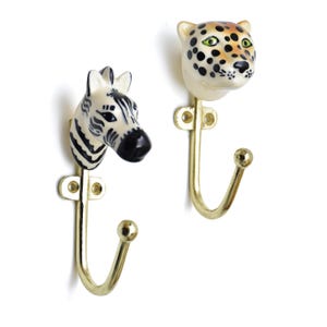 May include: Two decorative wall hooks. One hook features a zebra head with black and white stripes, and the other has a leopard head with black spots. Both hooks have a gold-colored metal hook.
