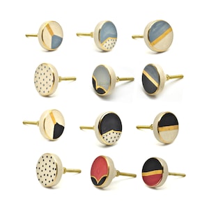 Puede incluir: Un conjunto de doce tiradores decorativos para armarios con vástagos de latón. Los tiradores presentan varios diseños geométricos en azul, negro, rojo y dorado, sobre un fondo crema. Los tiradores redondos tienen una estética moderna.