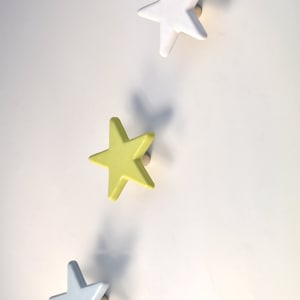 May include: Three star-shaped hooks in white, light blue, and yellow. The hooks are mounted on a white wall.