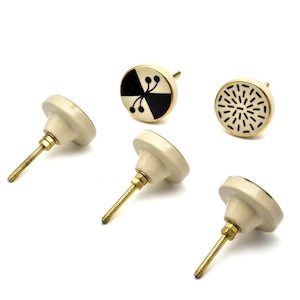 Op de afbeelding: Set van vijf keramische kastknoppen met gouden accenten. De knoppen hebben verschillende geometrische patronen in zwart en wit.