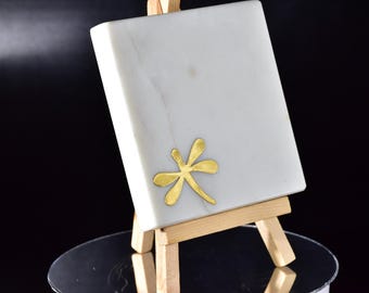 May include: A white marble coaster with a gold dragonfly design, displayed on a wooden easel.