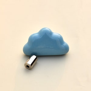 Può includere: Un pomello in ceramica a forma di nuvola azzurra con un tirante cilindrico in metallo argentato lucido. Il pomello è un elemento di design stravagante per mobili o decorazioni, adatto per cassetti o armadi.