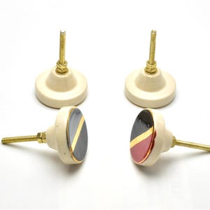 May include: Set of four ceramic cabinet knobs with a white base and a black and gold geometric design. Two knobs have a red accent.
