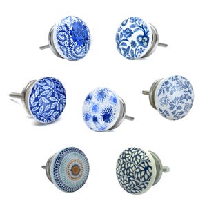 Puede incluir: Un conjunto de siete pomos de cerámica para armarios con diversos diseños florales y estampados en azul y blanco. Cada pomo tiene una base y un tornillo de metal plateado. Los pomos son redondos y presentan diferentes patrones, incluyendo flores, hojas y diseños abstractos.