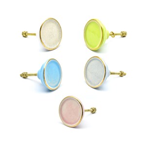 May include: Five ceramic cabinet knobs in various colours. Each knob features a round, flat face with a gold rim and a brass screw. The knobs are in shades of white, green, blue, grey, and pink. These knobs are suitable for adding colour to furniture.