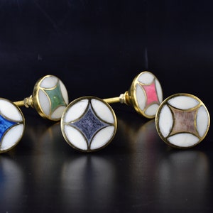May include: Four decorative cabinet knobs with a white base and a colourful geometric design. The knobs are made of brass and have a shiny finish.