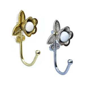 Pode incluir: Dois ganchos de parede decorativos. Um é dourado, o outro prateado. Cada gancho apresenta um design floral com um centro esférico branco. Os ganchos são feitos de metal e são projetados para pendurar objetos.