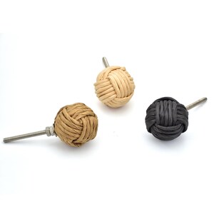 May include: Three decorative cabinet knobs. One is light tan, one is medium tan, and one is dark gray. Each knob is a woven sphere attached to a metal screw. The knobs are on a white background.