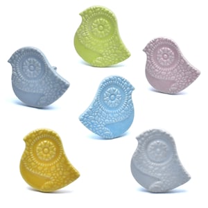 Könnte beinhalten: Sechs Keramik-Wandhaken in Vogelform in verschiedenen Pastellfarben, darunter hellblau, gelb, rosa und grün. Jeder Haken ist mit einem detaillierten Blumendesign verziert.