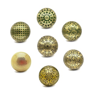 Może przedstawiać: Siedem dekoracyjnych gałek do szafek o skomplikowanych wzorach. Gałki mają kolory złota i zieleni, ze wzorami obejmującymi kwiatowe, geometryczne i tkane tekstury. Każda gałka ma kształt kuli.