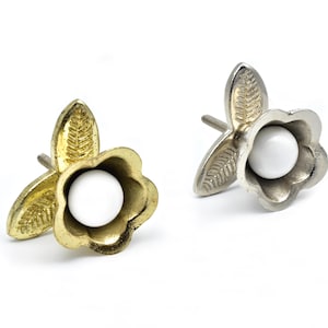 Puede incluir: Dos pomos de armario con forma de flor con un centro de cerámica blanca y acabados en oro y plata.