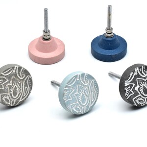May include: Five decorative cabinet knobs with a floral design. The knobs are made of concrete and have a metal screw. The knobs are in various colors, including pink, blue, gray, and black.