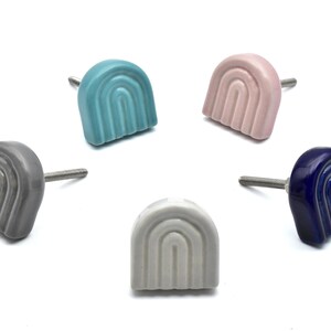 May include: Five ceramic rainbow-shaped cabinet knobs in different colors: gray, light blue, pink, white, and dark blue. Each knob has a silver screw.