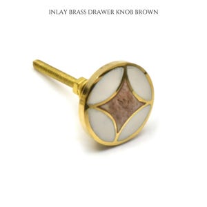 May include: A brass drawer knob with an inlay design. The knob features a gold finish, a white outer ring, and a brown diamond-shaped center. The text "INLAY BRASS DRAWER KNOB BROWN" is at the top.