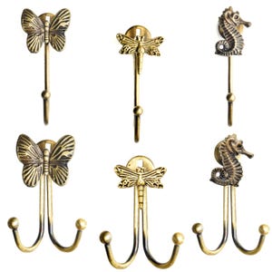May include: A selection of bronze-finished metal hooks. The hooks are adorned with butterfly, dragonfly, and seahorse motifs. Some have single hooks, others double. These decorative hooks are suitable for hanging items.