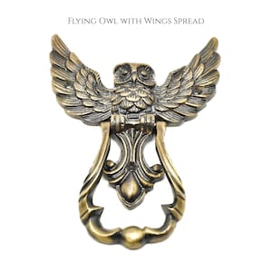 Peut inclure: Un heurtoir de porte de couleur bronze représentant un hibou détaillé aux ailes déployées. Le heurtoir a une poignée décorative et le texte "FLYING OWL WITH WINGS SPREAD" en haut. Les plumes du hibou et le design de la poignée sont richement détaillés.