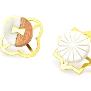 Op de afbeelding: Twee decoratieve knoppen met een gouden metalen frame. Eén knop is gemaakt van wit en bruin hout met een gouden accent. De andere knop is gemaakt van wit marmer met een zonnestralenontwerp.