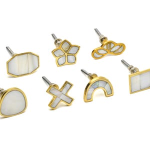 May include: Set of eight gold cabinet knobs with white mother of pearl inlays. The knobs are in various shapes, including a flower, a rectangle, a circle, a cross, and a rainbow.