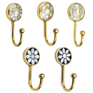 Puede incluir: Cinco colgadores de pared decorativos con tallos dorados y tapas circulares. Las tapas presentan diseños incrustados de nácar, incluyendo patrones geométricos y motivos florales. Los ganchos están diseñados para colgar objetos.