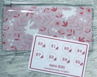 May include: A clear plastic zippered pouch with a pink floral and bunny pattern. A white card with circles labeled with dollar amounts and the text "save $36" is in front of the pouch. The text "mandysmonies_budgets" is also on the card.